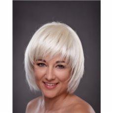 Uśmiechnięta kobieta z krótką, platynową peruką z grzywką na szarym tle.