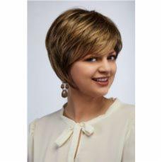 Uśmiechnięta kobieta z krótką, brązowo-blond peruką z asymetrycznym cięciem, w białej bluzce z wiązaniem pod szyją i z wiszącymi kolczykami na tle jasnego tła.