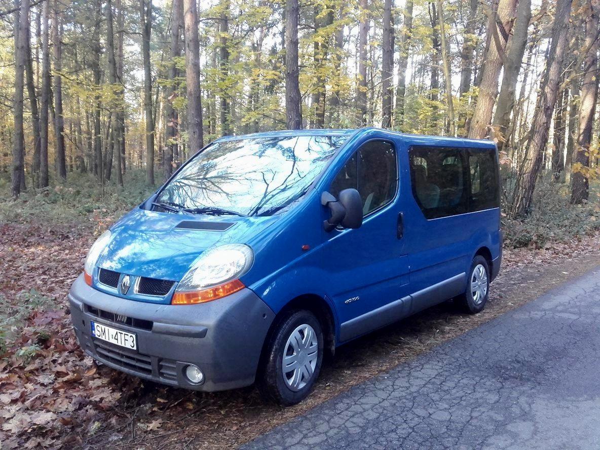 Niebieski van Renault Trafic zaparkowany na poboczu drogi w lesie, widoczne opadłe liście i drzewa w tle.