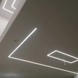 Sufit z zamontowanym oświetleniem LED w kształcie prostokątów i linii, widoczne kable zwisające z jednego z segmentów, drabina w rogu pomieszczenia.