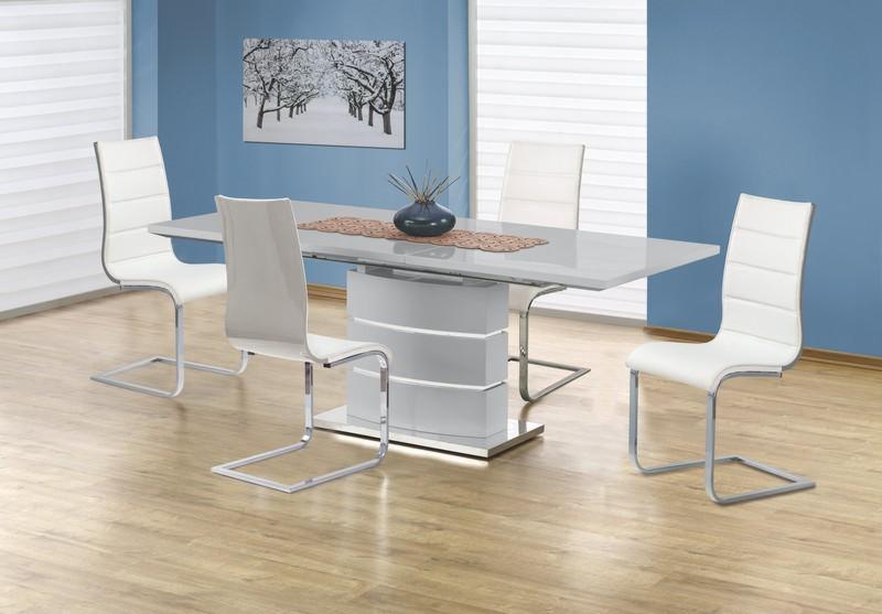 Biały, rozkładany stół z połyskiem i czterema białymi krzesłami na chromowanych nogach, ustawione w jadalni w Zielonce, z obrazem zimowego krajobrazu na ścianie.