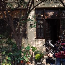 Paweł Kacprzak-produkcja filmowa, realizacja filmów reklamowych, promocyjnych, dokumentalnych - Ekipa filmowa kręci scenę przed budynkiem z drewnianymi oknami i roślinami, operator ustawia kamerę Alexa na statywie.