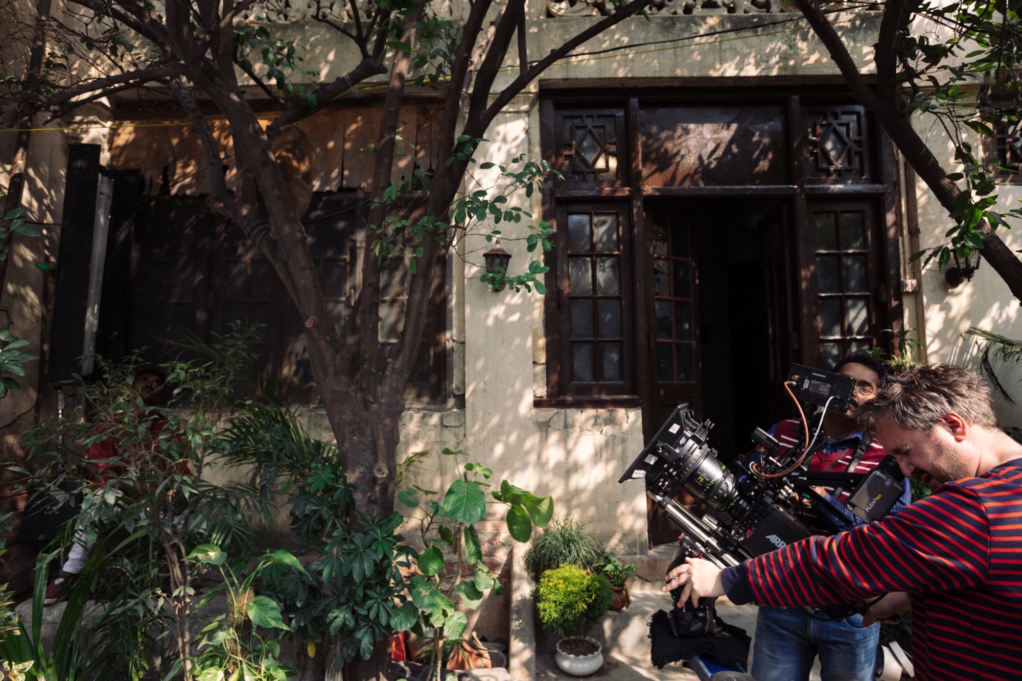 Ekipa filmowa kręci scenę przed budynkiem z drewnianymi oknami i roślinami, operator ustawia kamerę Alexa na statywie.