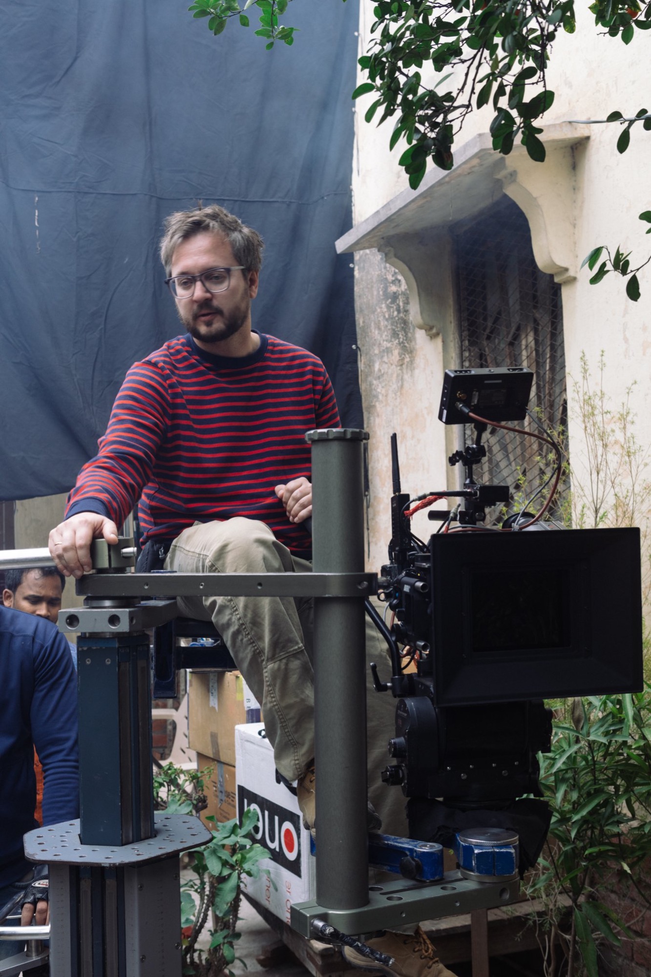 Operator kamery z Wrocławia obsługuje profesjonalną kamerę filmową na planie zdjęciowym z tłem z ciemnej tkaniny i budynkami w tle.