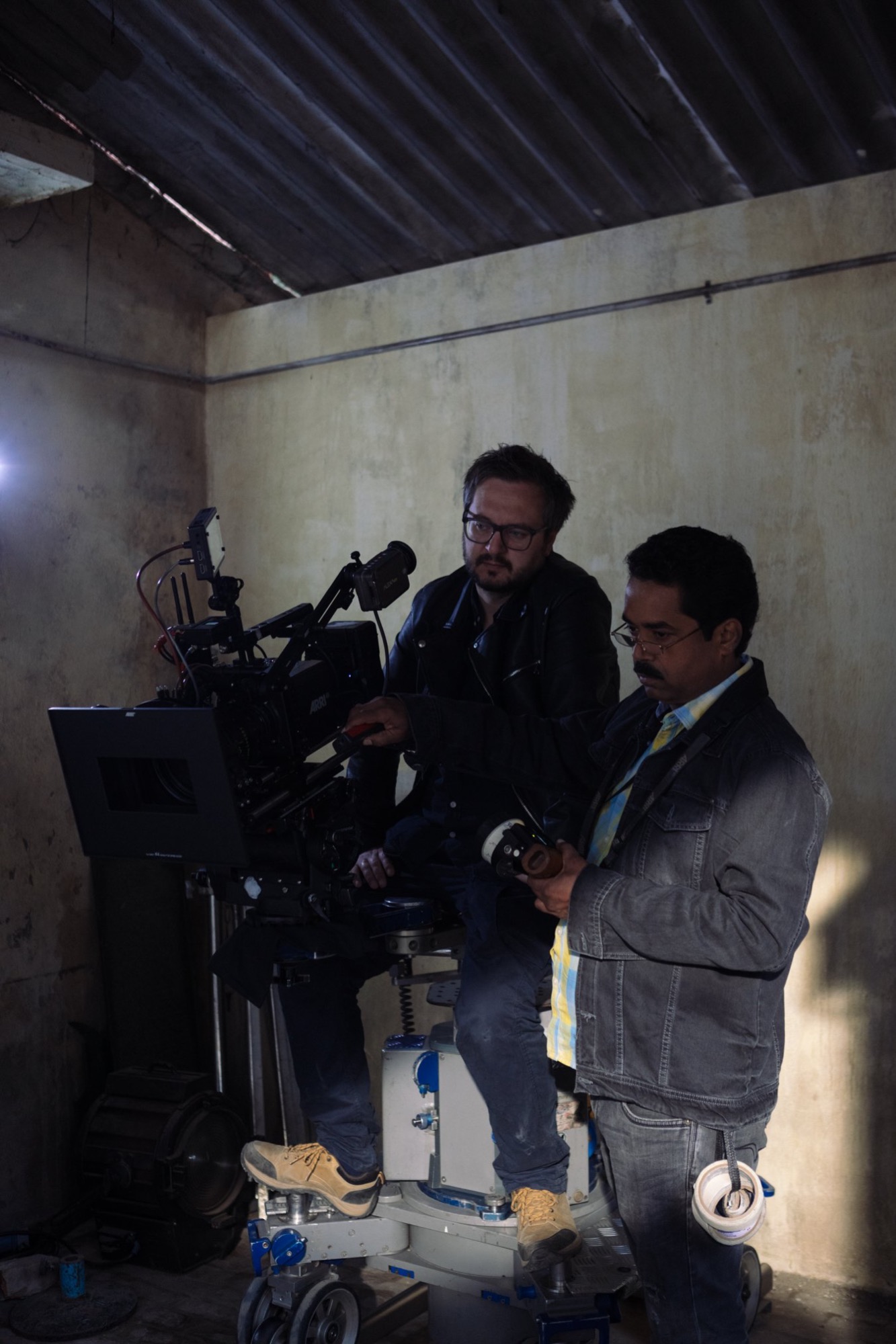 Dwóch mężczyzn obsługuje profesjonalną kamerę filmową na wózku dolly w surowym wnętrzu z blachą falistą na suficie.