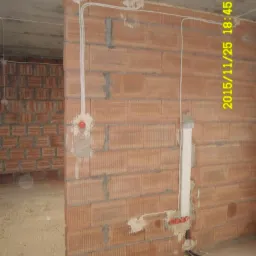 Wewnętrzna ściana z cegły z widocznymi przewodami elektrycznymi, puszkami instalacyjnymi i peszlem, w surowym stanie wykończenia wnętrza.