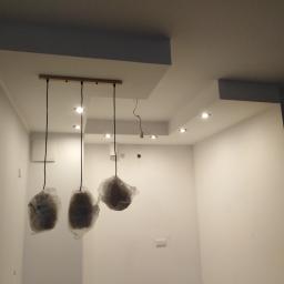 RBM Mariusz Bonk - Nowoczesne oświetlenie sufitowe z trzema lampami wiszącymi w folii ochronnej, sufit podwieszany z wbudowanymi punktami świetlnymi, świeżo pomalowane białe ściany w pustym pomieszczeniu.