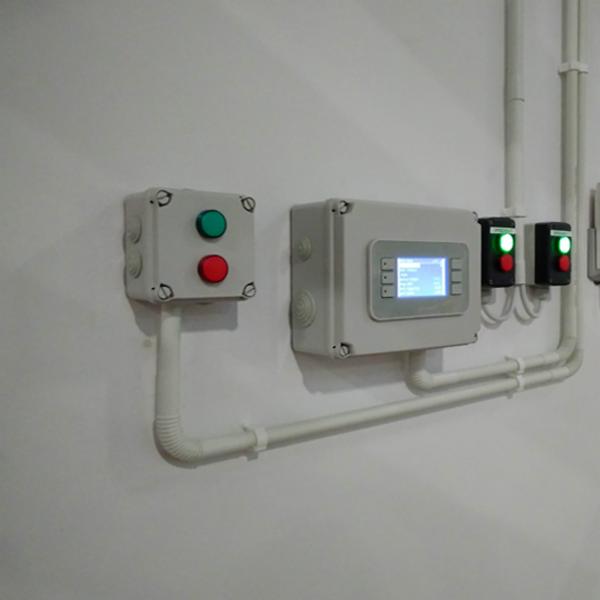 Panel sterowania z wyświetlaczem i przyciskami na ścianie, z widocznymi rurami instalacyjnymi.