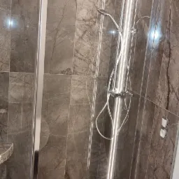 Nowoczesna kabina prysznicowa z deszczownicą i odpływem liniowym, wykończona płytkami imitującymi marmur i drewnem, oświetlona ledowym paskiem wzdłuż krawędzi.