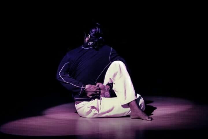 Osoba w sportowym stroju wykonuje skręt siedzący w Sieradzu, oświetlona punktowym światłem na drewnianej podłodze.