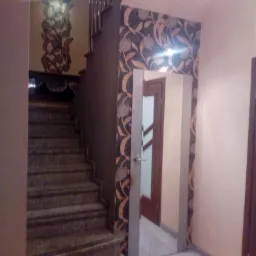 Klatka schodowa z marmurowymi schodami i dekoracyjną tapetą w kwiatowe wzory na ścianie oraz obramowaniu drzwi.