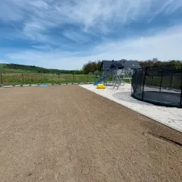 Przygotowany teren pod trawnik z rolki, widoczny plac zabaw z trampoliną i huśtawką, tło stanowi zielony krajobraz.