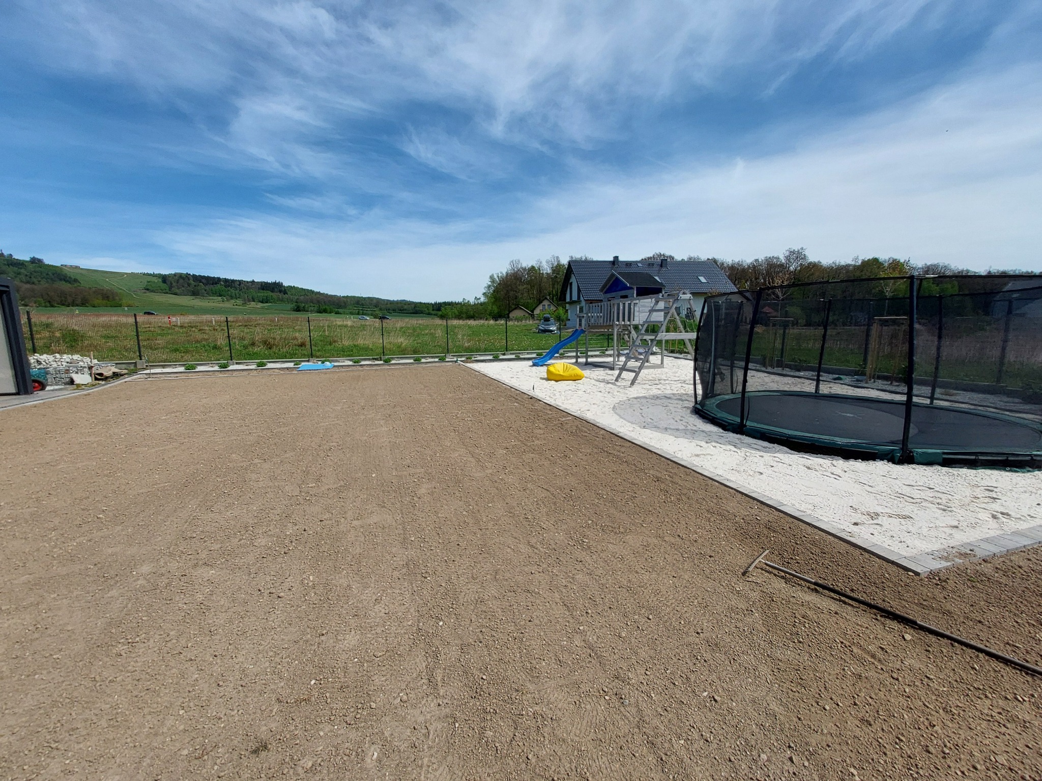 Przygotowany teren pod trawnik z rolki, widoczny plac zabaw z trampoliną i huśtawką, tło stanowi zielony krajobraz.