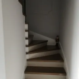 Kręte schody z drewnianymi stopniami i białymi podstopnicami, prowadzące w górę, z dekoracyjnym żołnierzykiem na jednym ze stopni.