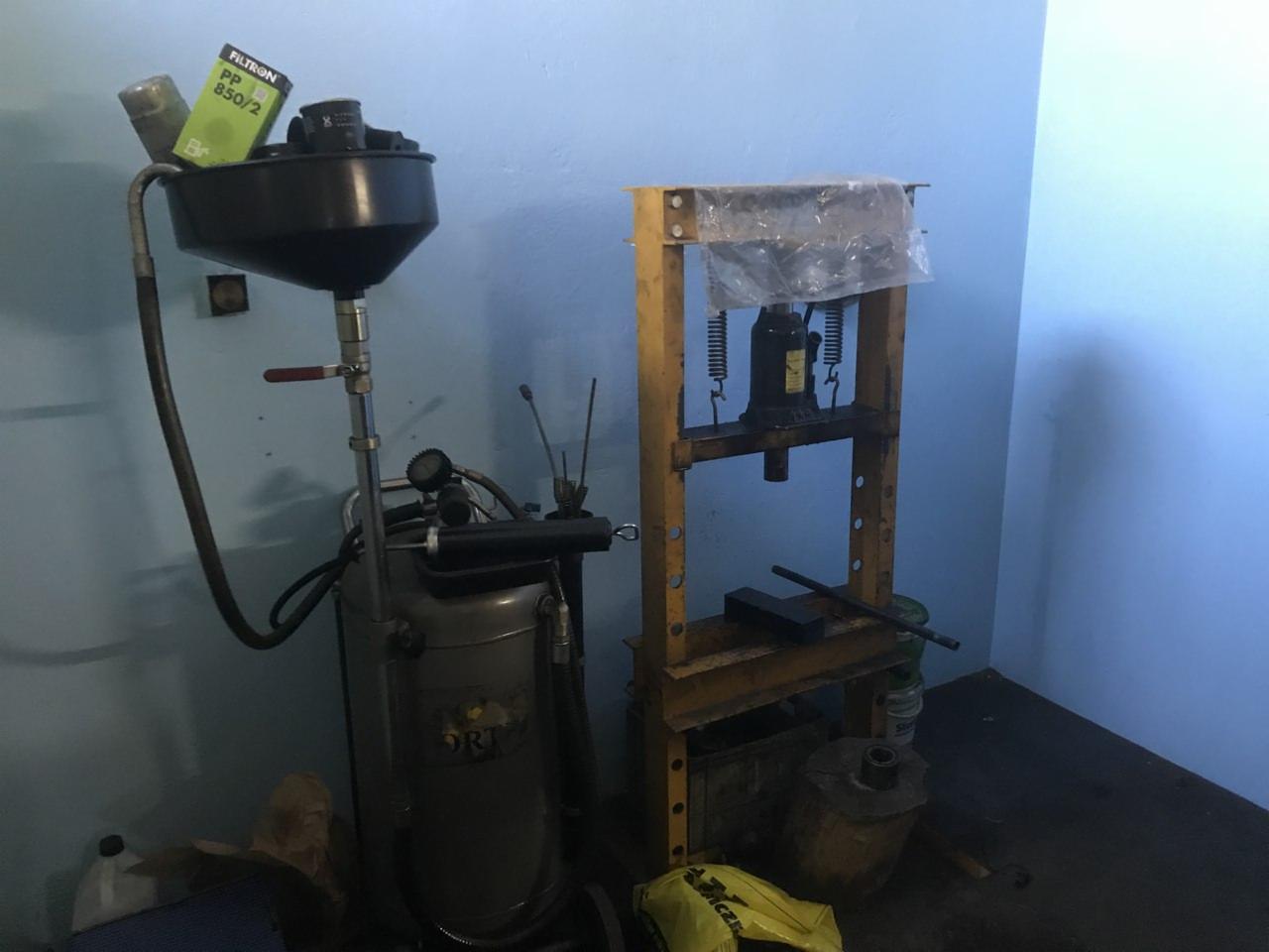 Warsztatowy widok: urządzenie do wymiany oleju z filtrami Filtron na górze oraz prasa hydrauliczna w tle, na tle błękitnej ściany.