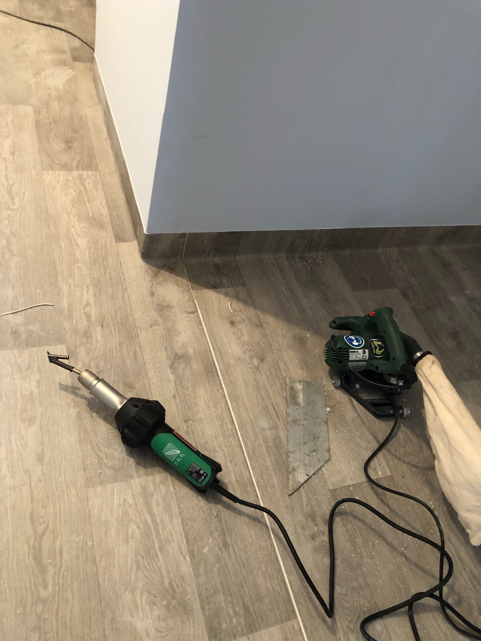 Przygotowanie podłoża pod posadzkę: frezarka i opalarka Leister na panelach imitujących drewno, widoczny fragment ściany.