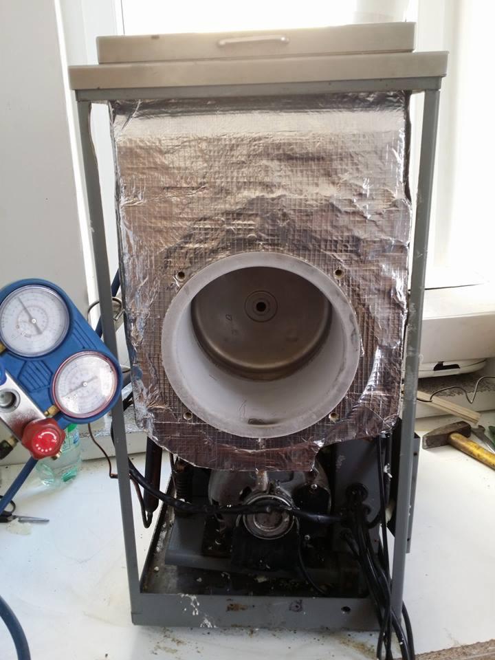 Demontaż lub naprawa urządzenia z izolacją termiczną, widoczne manometry, przewody i narzędzia na stole warsztatowym.