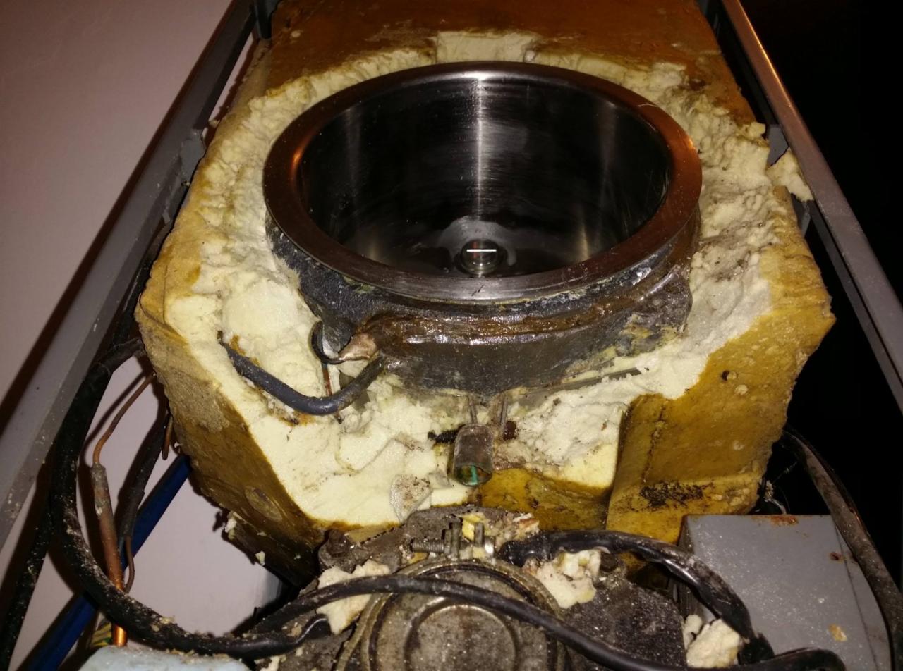 Wnętrze klimatyzatora z widoczną izolacją, metalowym zbiornikiem i przewodami, ukazujące stan zużycia i potencjalną potrzebę serwisu.