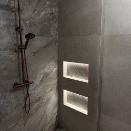 Fachowiec - Wykończona łazienka z marmurowymi płytkami, miedzianą armaturą prysznicową i podświetlanymi wnękami w ścianie. Minimalistyczny design z odpływem liniowym.
