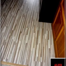 Ułożone panele podłogowe w odcieniach beżu i brązu, wzór imitujący drewno, widoczne przy progu drzwi, z listwą przypodłogową.