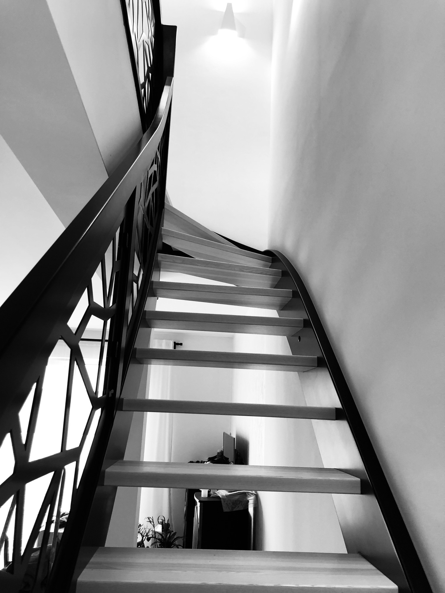 Nowoczesne schody z drewnianymi stopniami i metalową balustradą o geometrycznym wzorze, widok z dołu w czerni i bieli.