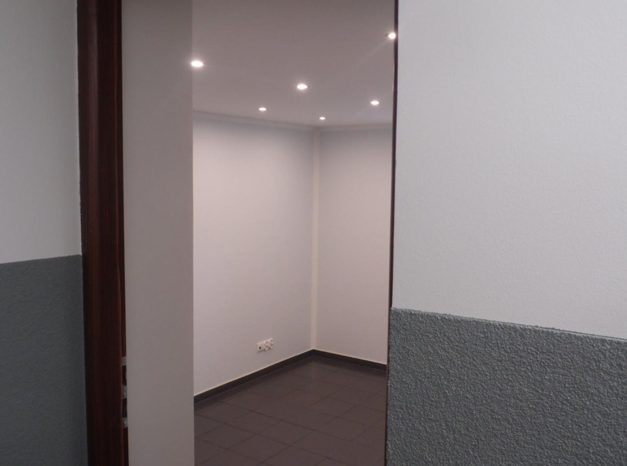 Wnętrze biura po adaptacji piwnicy, widoczne świeżo pomalowane ściany w odcieniach szarości i brązowa podłoga z płytek, oświetlenie punktowe w suficie.