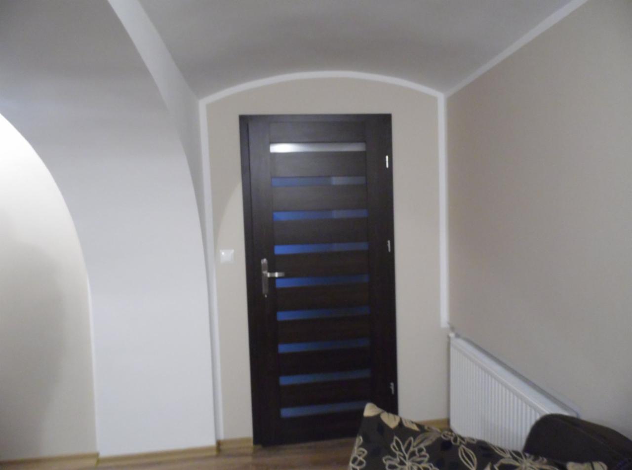 Ciemne, nowoczesne drzwi wewnętrzne z poziomymi, niebieskimi przeszkleniami, zamontowane w odnowionym pomieszczeniu z łukowym przejściem i świeżo pomalowanymi ścianami w odcieniach beżu i bieli.