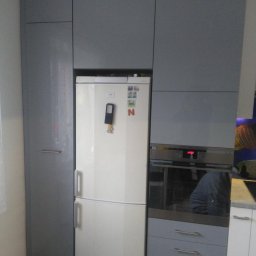 P.P.H.U. Meyer - Szare szafki kuchenne na wymiar z wbudowaną białą lodówką i piekarnikiem, widoczne magnesy na lodówce.