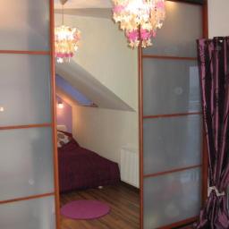 P.P.H.U. Meyer - Szafa przesuwna z lustrzanymi drzwiami odbijająca wnętrze pokoju na poddaszu z fioletowym dywanikiem i łóżkiem, widoczna dekoracyjna lampa z motywem kwiatowym.