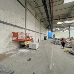 IS BUD® Mykola Mostovyi - Wnętrze hali w trakcie prac wykończeniowych: ściany z bloków, podnośnik koszowy, materiały budowlane. Widoczne instalacje pod sufitem i oświetlenie.