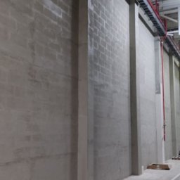 IS BUD® Mykola Mostovyi - Surowa ściana z betonu komórkowego z pionowymi wzmocnieniami, widoczne instalacje pod sufitem. Minimalistyczne wykończenie hali przemysłowej w szarościach.