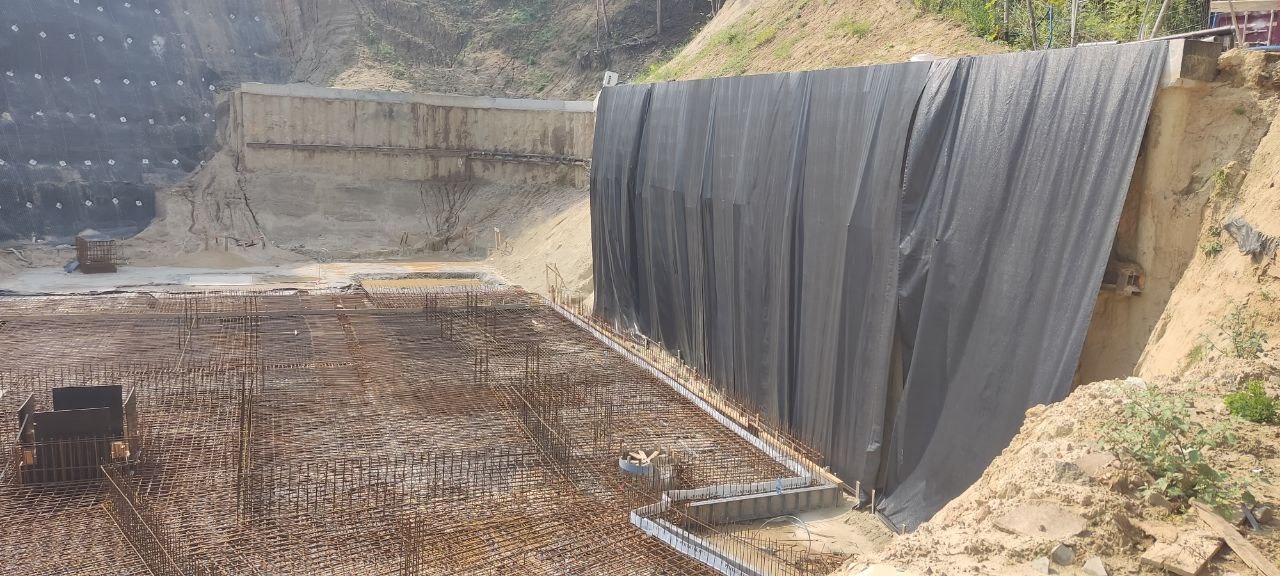 Rozległy widok na plac budowy z siatką zbrojeniową i zabezpieczeniem skarpy. Widoczne elementy konstrukcyjne i przygotowanie terenu pod dalsze prace.