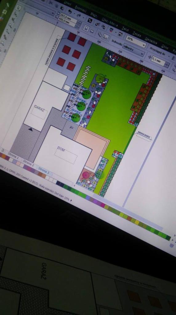 Widok z bliska na ekran komputera prezentujący kolorowy, szczegółowy plan zagospodarowania terenu wokół domu z garażem, uwzględniający zieleń, ścieżki i elementy małej architektury, wykonany...