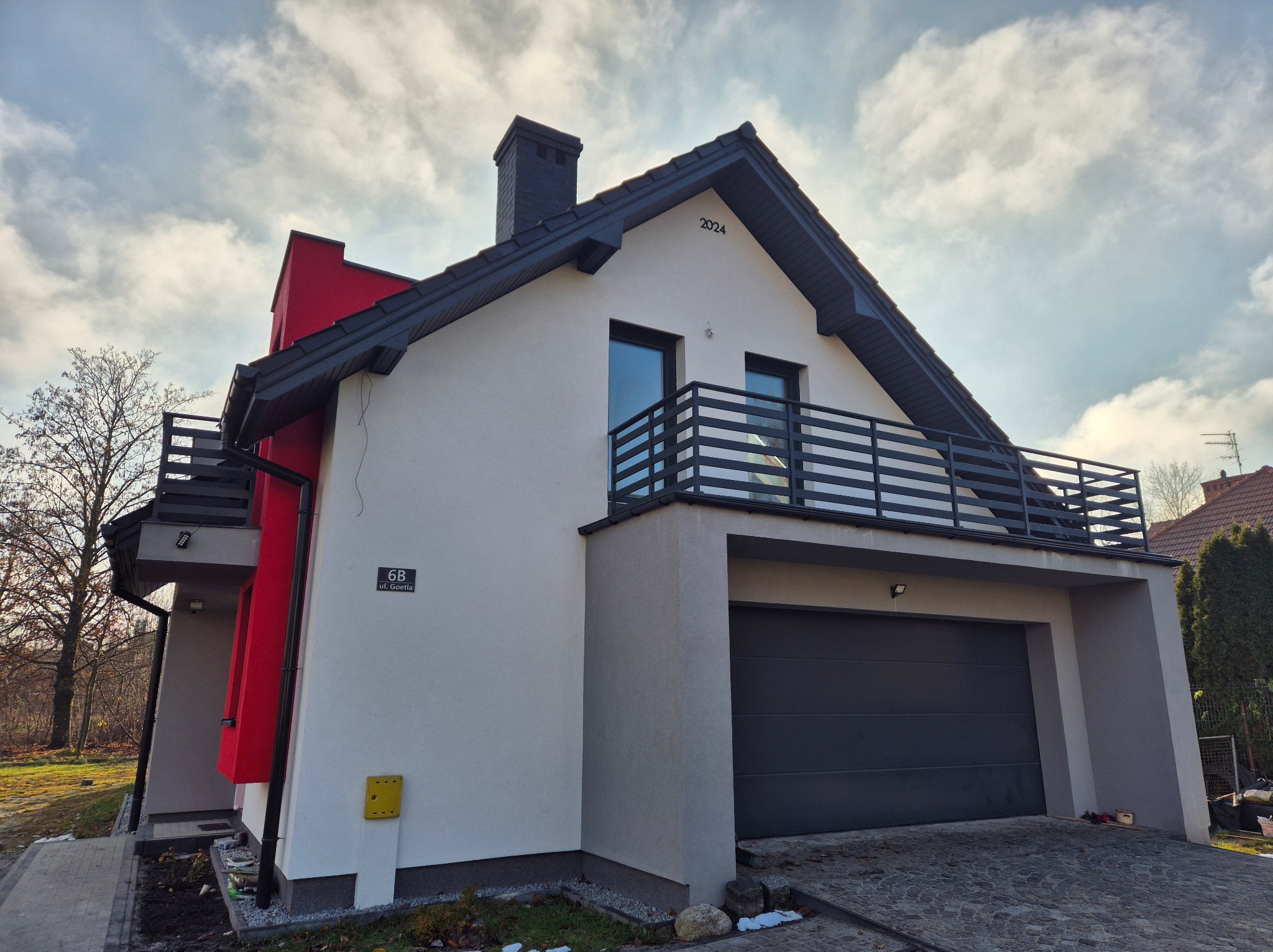 Nowoczesny dom jednorodzinny z balkonem zabezpieczonym czarną, metalową balustradą, widok z zewnątrz w pochmurny dzień.