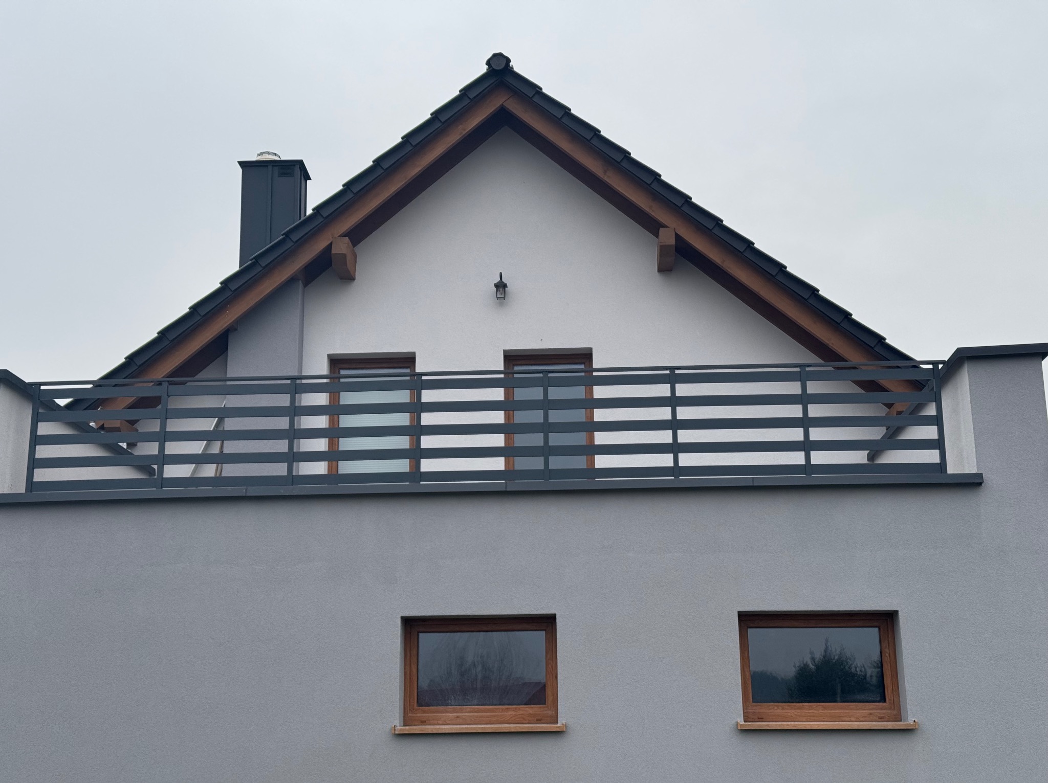 Szary dom jednorodzinny w Psarach z balkonem zabezpieczonym poziomą, metalową konstrukcją.