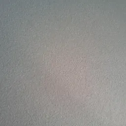 Szara ściana z delikatną strukturą, oświetlona z dołu, ukazująca subtelne cieniowanie.