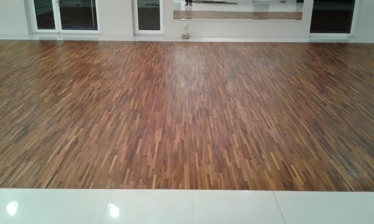 Świeżo ułożony parkiet z ciemnego drewna w jasnym pomieszczeniu z białymi ścianami i lustrami, widoczne odbicie osoby w lustrze.