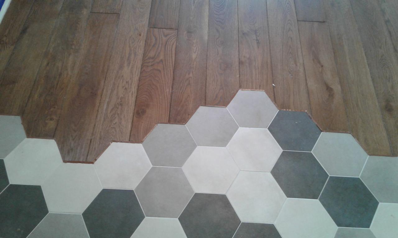 Połączenie układanego parkietu z szarymi, heksagonalnymi płytkami podłogowymi w trakcie prac wykończeniowych.