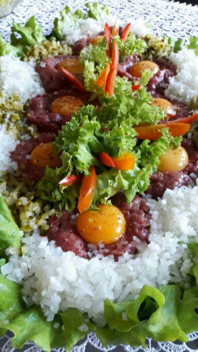 Wykwintna kompozycja tatara wołowego z surowym żółtkiem, ryżem, sałatą i papryką na białej koronkowej serwecie.