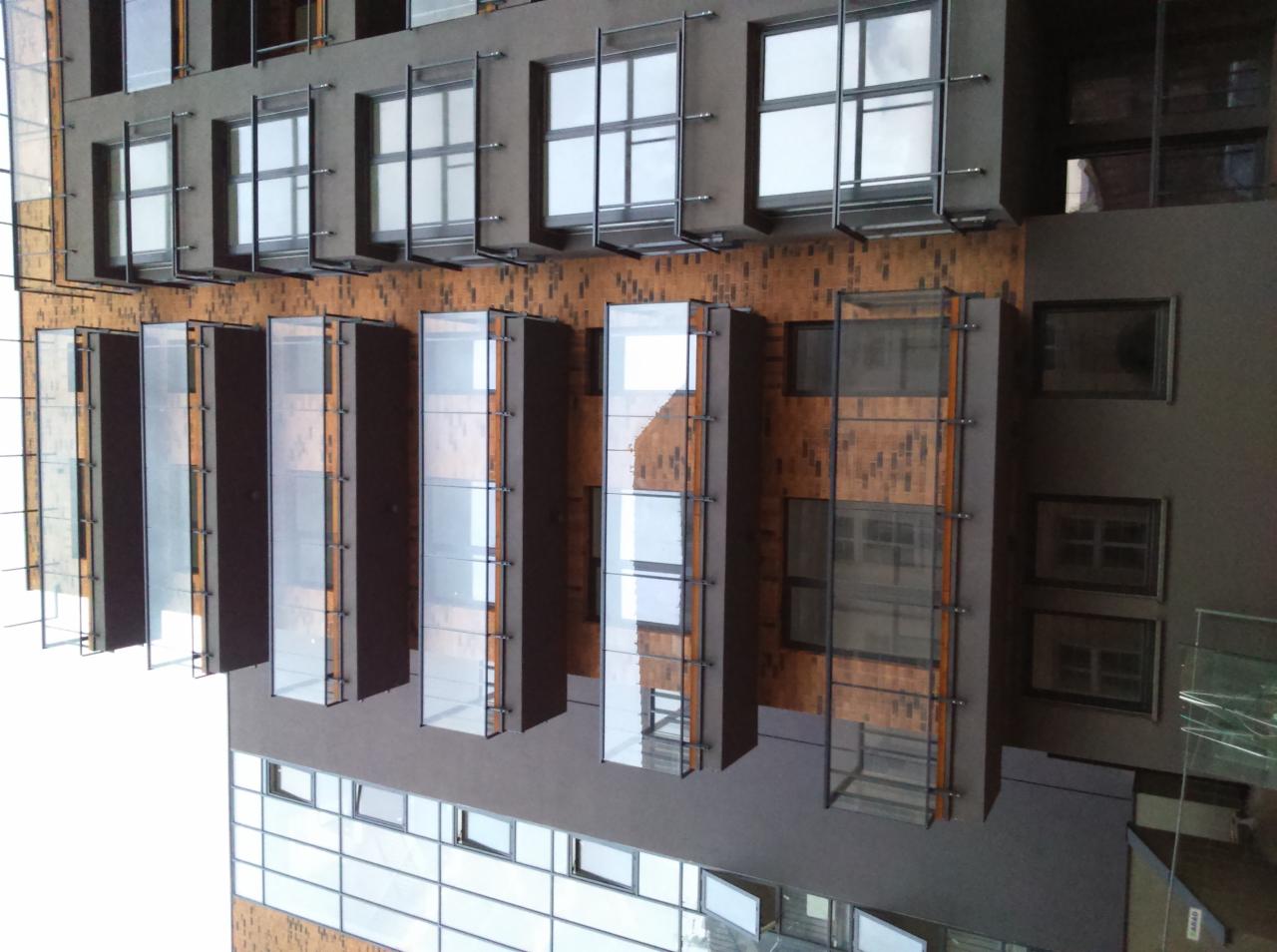 Nowoczesna fasada budynku z elementami z płyt warstwowych, widoczne szklane panele i okna z metalowymi ramami, na tle ceglanej ściany.