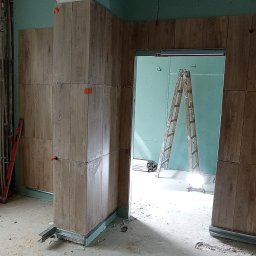 EMS SYSTEM - Montaż płyt imitujących drewno na ścianach z płyt kartonowo-gipsowych w trakcie remontu, widoczna drabina i narzędzia pracy.