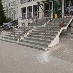 EMS SYSTEM - Zewnętrzne schody kamienne z metalową balustradą prowadzące do budynku z zielonymi akcentami, widoczne ślady po remoncie na chodniku.