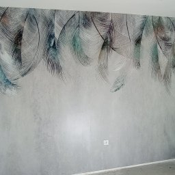 EMS SYSTEM - Ściana po malowaniu z dekoracyjnym motywem piór w odcieniach szarości i turkusu, widoczne gniazdko elektryczne i surowy fragment ściany w trakcie remontu.