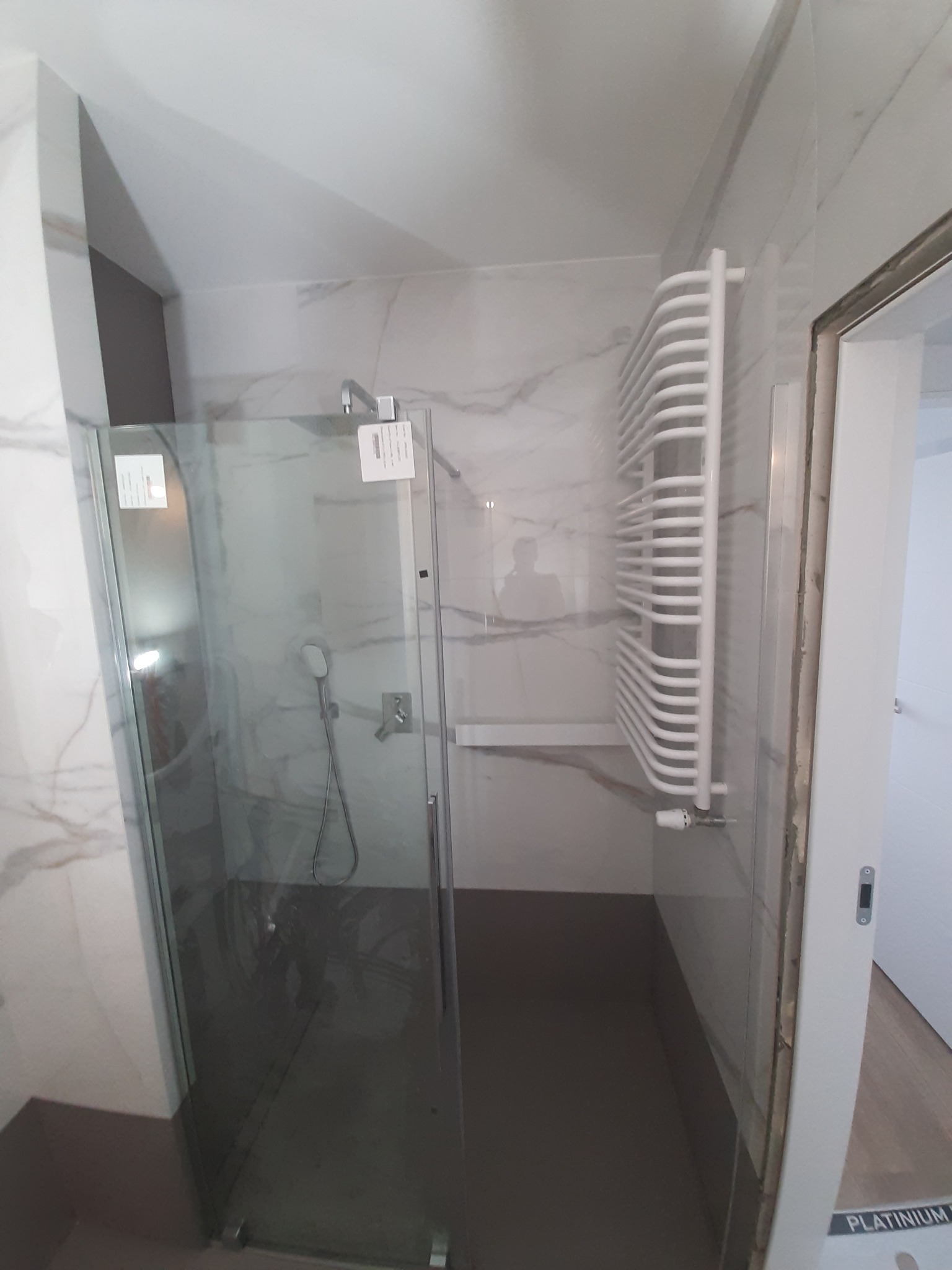 Nowoczesna kabina prysznicowa z szklanymi drzwiami, biały grzejnik drabinkowy i marmurowe płytki ścienne w wykończonej łazience.