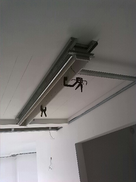 Montaż sufitu podwieszanego z płyt kartonowo-gipsowych, widoczne metalowe profile, płyta G-K, uchwyty montażowe i fragment instalacji elektrycznej.