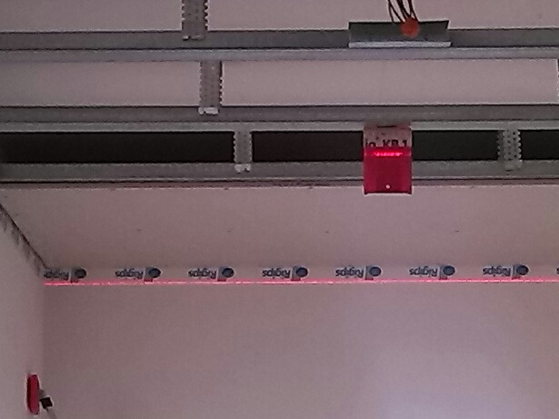 Montaż sufitu podwieszanego z płyt karton-gips, widoczna konstrukcja metalowa, płyta Rigips, oraz laserowy niwelator wyznaczający poziom na ścianie.