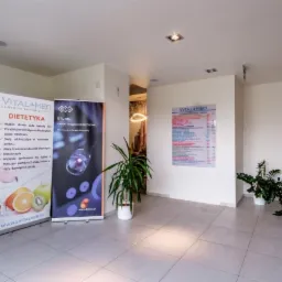 Jasne wnętrze centrum rehabilitacji z recepcją, schodami i roll-upami reklamowymi dietetyki i laseroterapii BTL-HIL.