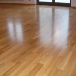 Świeżo wycyklinowana, lakierowana podłoga parkietowa z widocznymi refleksami światła, ułożona w jodełkę, w jasnym, pustym pokoju.