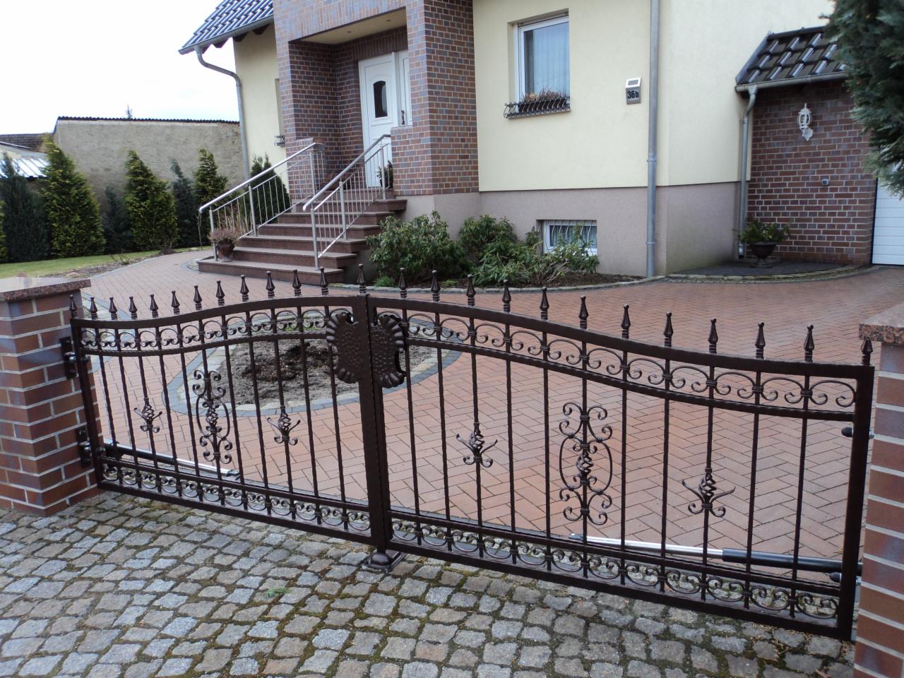 Kuta, dwuskrzydłowa brama wjazdowa z automatyką, zamontowana na posesji z brukowanym podjazdem i domem z ceglanym wykończeniem.