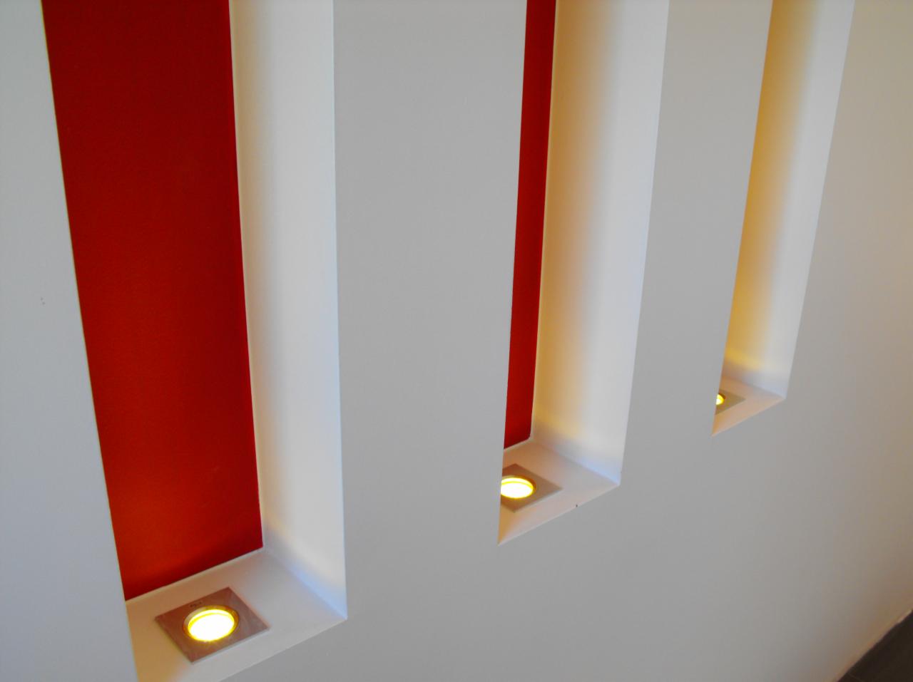 Nowoczesne oświetlenie ścienne z wnękami: czerwona ściana akcentująca i wbudowane punktowe lampy LED w białych, minimalistycznych obudowach, tworzące geometryczny wzór.